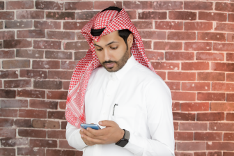 صوة رجل سعودي بالثوب التقليدي يقف وهيتصفح هاتفه المحول