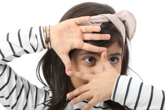 طفلة صغيرة تضع يديها حول عينها اليمني وكأنها تلتقط صورة