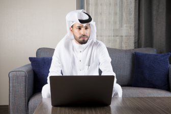 رجل أعمال عربي خليجي، يجلس على كنبة، يعمل من المنزل وينظر إلى يساره