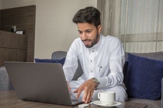 رجل سعودي يستخدم الكمبيوتر المحمول ويشرب القهوة
