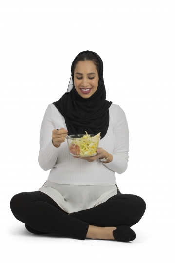 إمرأة عربية سعودية حامل مبتسمة تحمل طبق خضروات في يديها وتنظر اليه