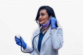 تظهر الصورة طبيبة فلبينية شابة تستخدم سماعة الطبيب أثناء ارتدائها قناع وجه وقفازات يمكن التخلص منها من أجل السلامة