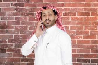 صورة لرج سعودي بالثوب التقليدي يقف أثناء حيثه عل الجوال