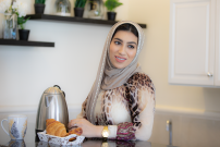 امرأة عربية ترتدي الحجاب تبتسم وتنظر إلى اليمين أثناء تحضير وجبة الافطار والشاي بالمنزل