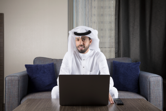 رجل أعمال عربي سعود مبتسم يجلس على كبة يرتدي ثوب أبيض وغترة ويظر إلى يمينه