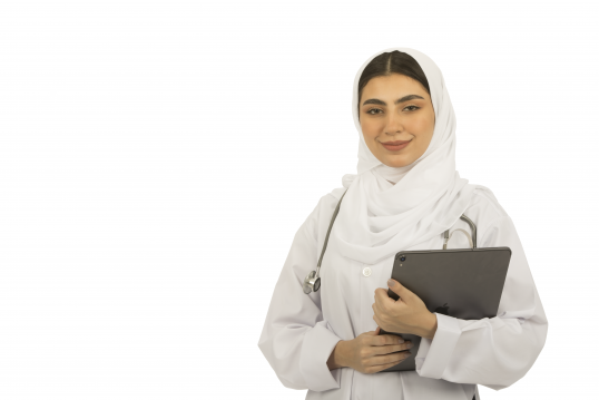 صورة لطبيبة سعودية ترتدي سماعة الطبيب وتبتسم للكاميرا.دكتورة عربية ترتدي الحجاب وتحمل بيدها كمبيوتر لوحي -تابلت