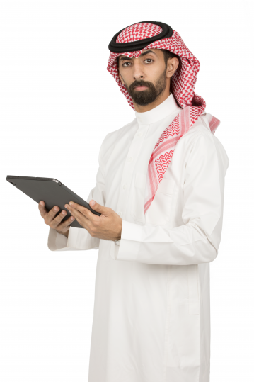 رجل عربي سعودي يرتدي ثوب أبيض يقف بوضع جانبي يحمل آيباد و ينظر إلى الأمام