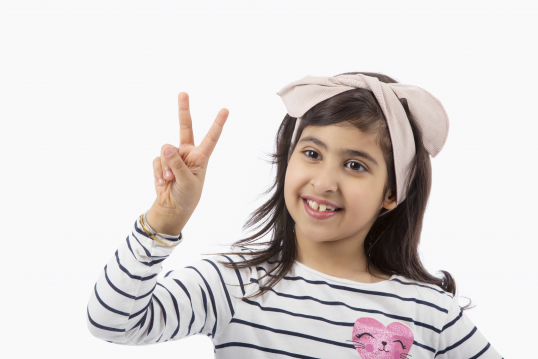 صوة لطفلة  سعوية شاة ترفع شعار السلام. فتاة صغيرة مبتهجة تقوم بعلمة يد النصر وهي متسمة.