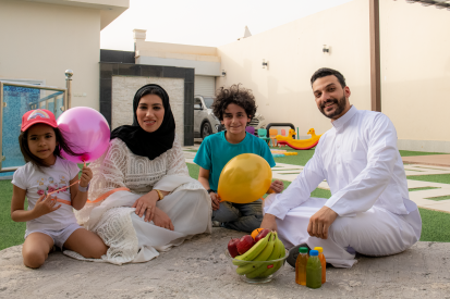 عائلة عربية سعودية تجلس في حديقة المنزل لقضاء وقت ممتع ويبتسمون أثناء النظر إلى الكاميرا