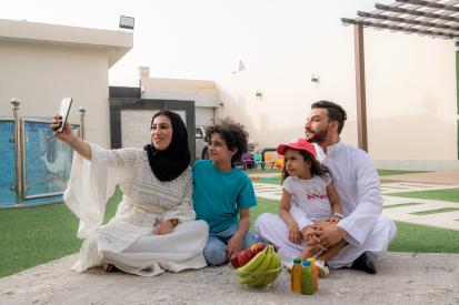 امرأة عربية سعودية حجبة تجل مع عائلتها في حدقة المنل بينما تحمل الجوال لإلتقاط صورة تمعهم معاً