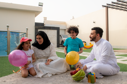 عائلة عربية سعودية تستمتع بوقتها في حديقة المنزل وأبنائهم يحملون البالونات